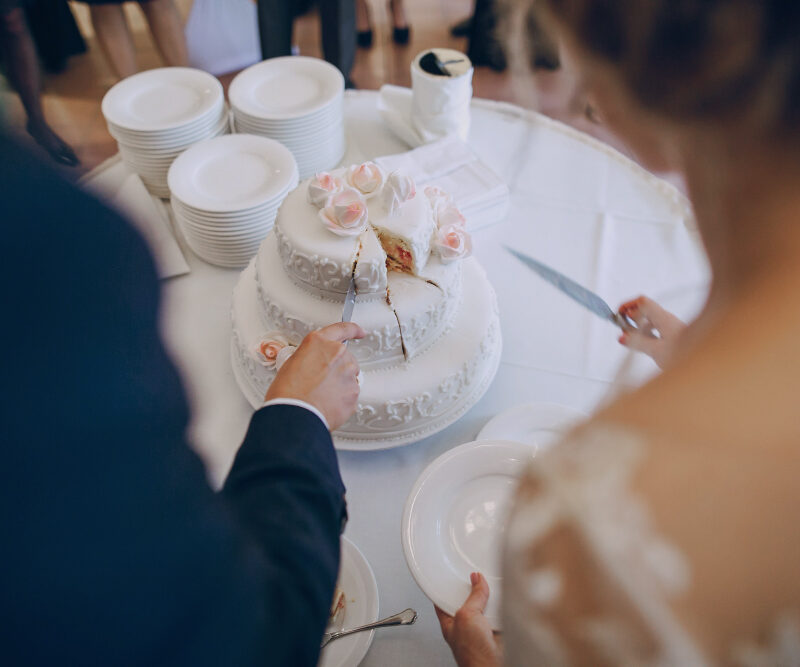 Sposi durante il taglio della torta nuziale con servizio di catering per matrimoni e tavolo elegante per il ricevimento.